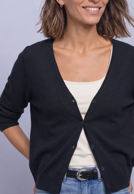Cardigan à col en V et patte de boutonnage darkest blue Buste d’une femme souriante en cardigan noir sur débardeur blanc, jean bleu et ceinture.