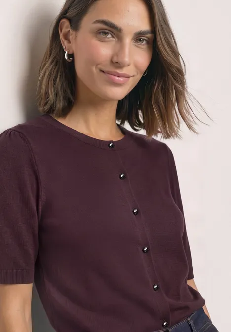 Kurzarm Cardigan mit Rundhals und Knöpfen rustic rouge Eine Frau mit schulterlangem Haar trägt eine weinrote Kurzarmstrickjacke mit schwarzen Knöpfen und lächelt.
