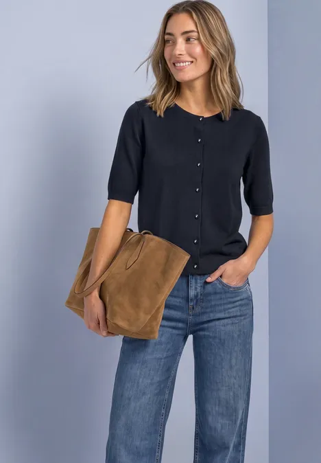 Vrouw in donkerblauw kort vest, spijkerbroek en bruine tas.