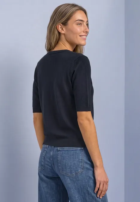 Vrouw in zwart T-shirt met halflange mouwen en blauwe jeans, zij-achteraanzicht.