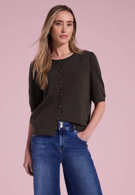 Vrouw voor een roze achtergrond in een zwarte blouse met knopen en een blauwe spijkerbroek