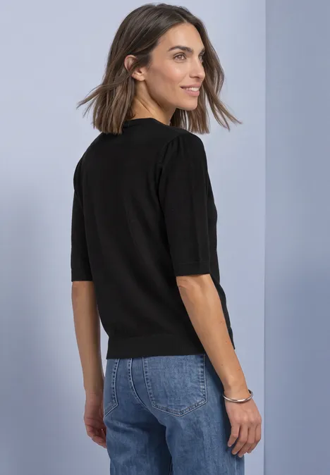 Vrouw in zwart shirt en jeans kijkt over haar schouder.