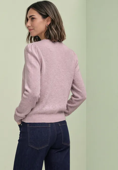 Frau in rosa Pullover und dunkler Jeans, seitlich vom Rücken zu sehen, vor hellem Hintergrund.