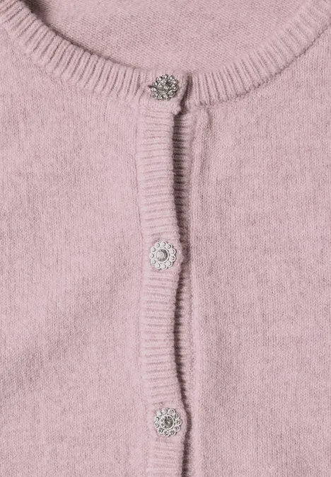 Nahaufnahme eines rosa Strickcardigans mit Rippenbündchen und funkelnden Schmuckknöpfen.
