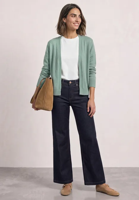 Femme en t-shirt blanc, gilet vert doux, jean large bleu foncé, mocassins et sac ocre.