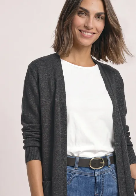 Frau trägt weiße Bluse, graue Strickjacke, Jeans und schwarzen Gürtel mit goldener Schnalle.