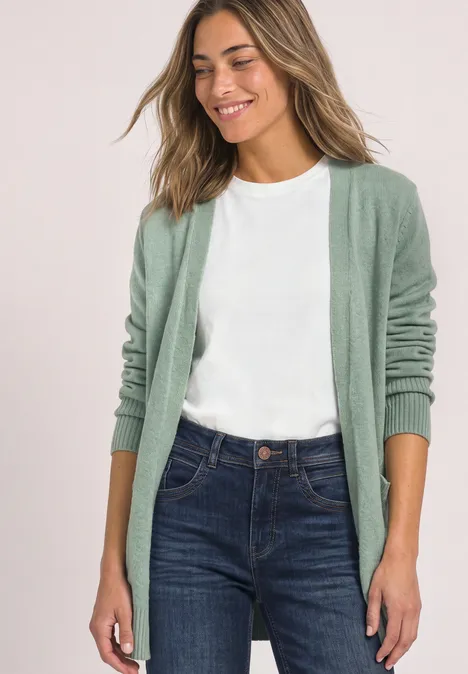 Femme souriante portant un t-shirt blanc, un jean bleu et un gilet vert