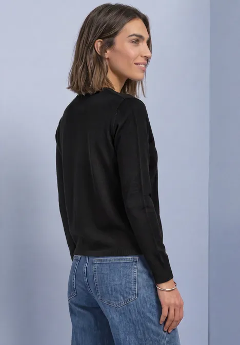 Offener Cardigan in Unifarbe Black Frau in schwarzem Pullover und blauer Jeans, von hinten vor neutralem Hintergrund.