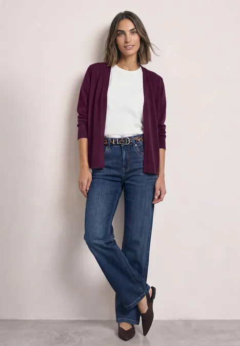 Offener Cardigan in Unifarbe berry maroon Eine Frau posiert vor neutralem Hintergrund, trägt weißen T-Shirt, bordeauxfarbenen Cardigan, blaue Jeans und Loafers.