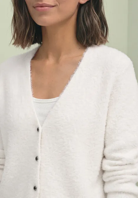 Frau in weißer flauschiger Strickjacke und weißem Top, Close-up auf Oberkörper und Arme.