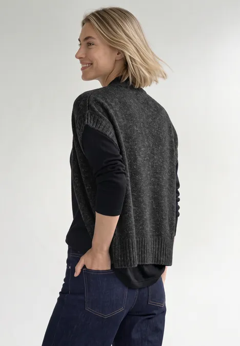 Dropped Shoulder Cardigan mit Turtle Neck und Zipper armor grey mel. Eine Frau in dunklen Jeans, schwarzem Langarmshirt und grauer Strickweste geht seitlich, lächelnd.