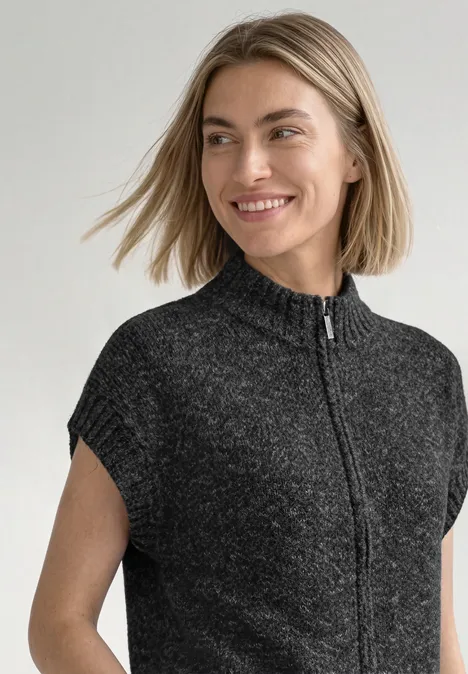 Dropped Shoulder Cardigan mit Turtle Neck und Zipper armor grey mel. Eine lächelnde Frau trägt einen kurzen, dunkelgrauen Strickpullover mit Stehkragen und Reißverschluss.