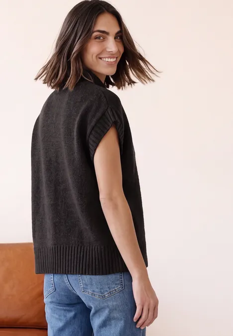 Dropped Shoulder Cardigan mit Turtle Neck und Zipper black coffee mel. Frau in dunkelgrauem, ärmellosem Strickpullunder blickt über die Schulter und lächelt.