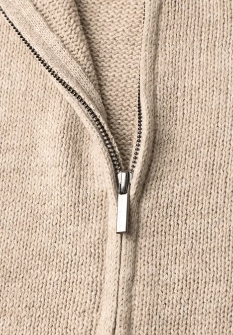 Nahaufnahme eines beigen Strickpullovers mit offenem silberfarbenem Reißverschluss