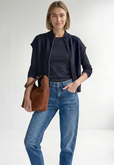 Dropped Shoulder Cardigan mit Turtle Neck und Zipper indigo night mel. Eine lächelnde Frau trägt blaue Jeans, ein dunkelblaues Shirt, eine Bomberjacke und eine braune Tasche.