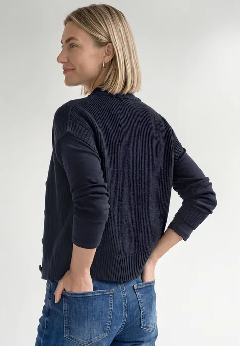 Dropped Shoulder Cardigan mit Turtle Neck und Zipper indigo night mel. Frau mit kurzem blondem Haar trägt dunkelblauen Pullover und Jeans, steht seitlich mit Händen an den Hüften.