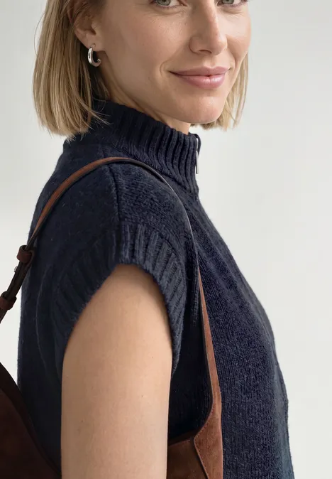 Dropped Shoulder Cardigan mit Turtle Neck und Zipper indigo night mel. Frau im dunkelblauen ärmellosen Rollkragenpullover mit brauner Tasche.
