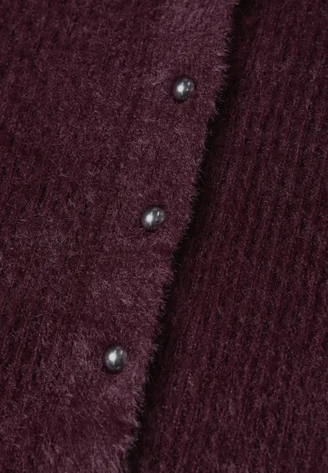 Close-up van een bordeauxrode, pluizige gebreide cardigan met ribstructuur en glanzende knopen.