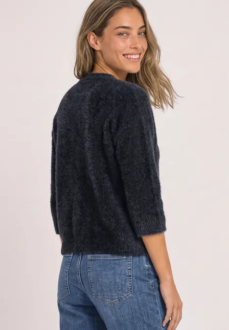 Frau im schwarzen, flauschigen Pullover und Jeans schaut lächelnd über die Schulter.