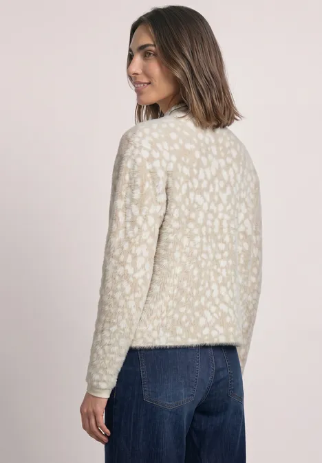 Vrouw in profiel met crèmekleurige trui met patroon en blauwe spijkerbroek.
