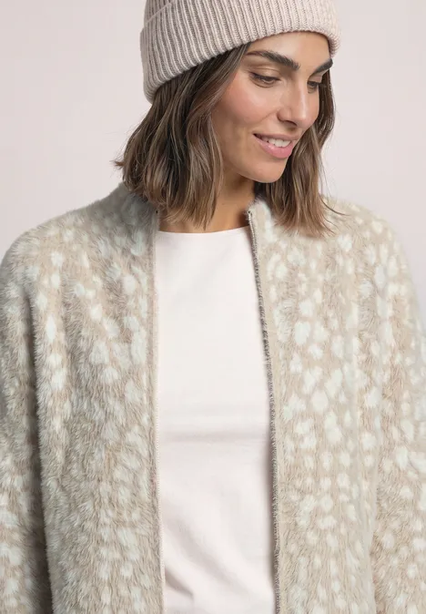 Vrouw met lichtgrijze gebreide muts en pluizig beige-crème cardigan met luipaardprint op wit shirt.