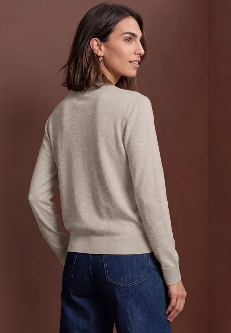 Femme de dos en pull beige et jean bleu foncé devant un fond marron