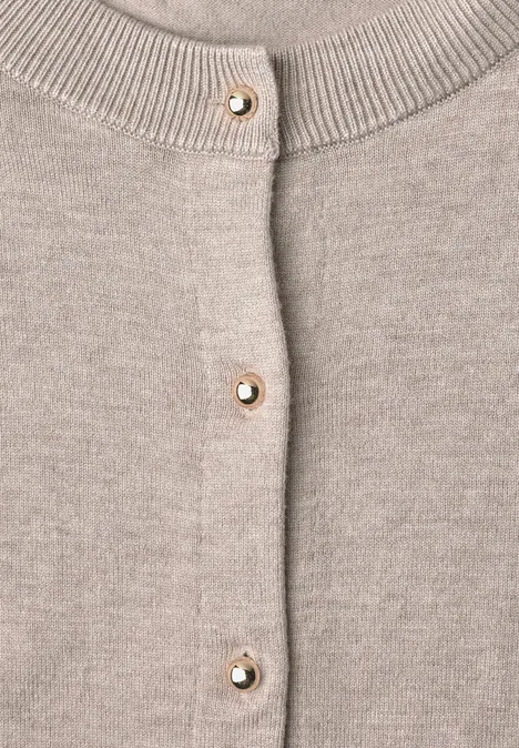Gros plan d’un gilet beige en maille avec boutons dorés ornés de perles.