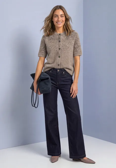 Femme portant un gilet gris à manches courtes, un pantalon large noir, des chaussures marron et un sac noir.