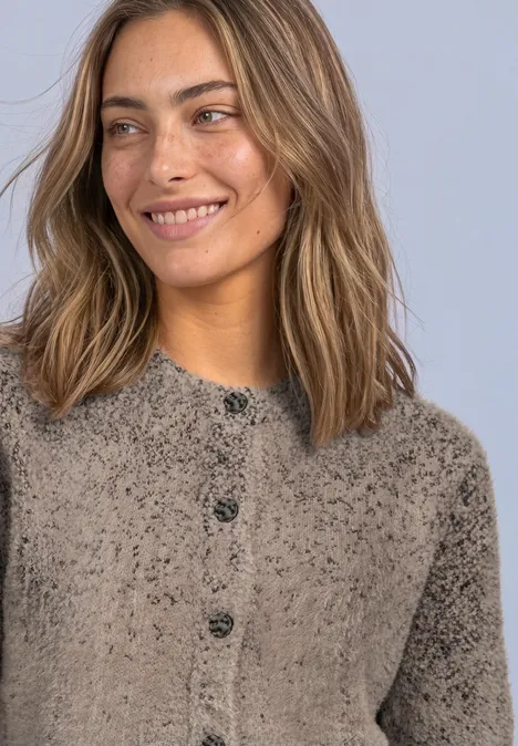 Une femme souriante avec un pull duveteux à boutons, cheveux clairs, pose détendue.