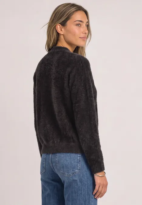 Frau von hinten mit schwarzem, flauschigem Pullover und blauen Jeans vor hellem Hintergrund.