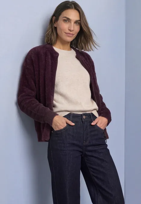 Vrouw in bordeaux vest, lichte trui en jeans voor een lichte achtergrond