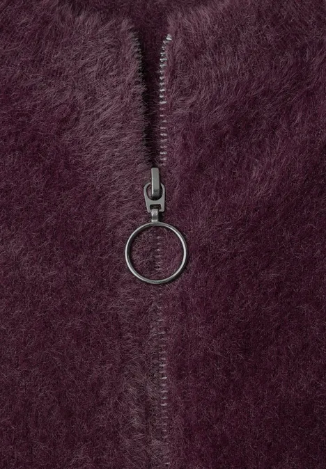 Close-up van paars pluizig materiaal met een rits en ronde ring als ritstrekker.