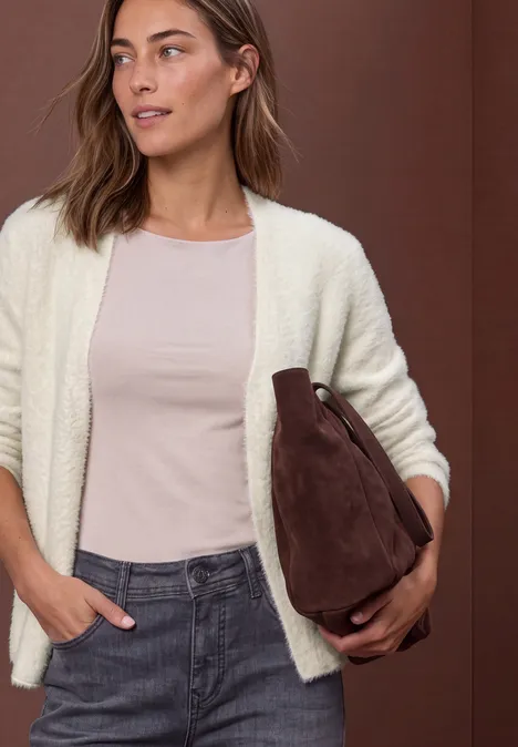 Femme en gilet clair, t-shirt rose et jean, tenant un sac marron en suédine sous le bras.
