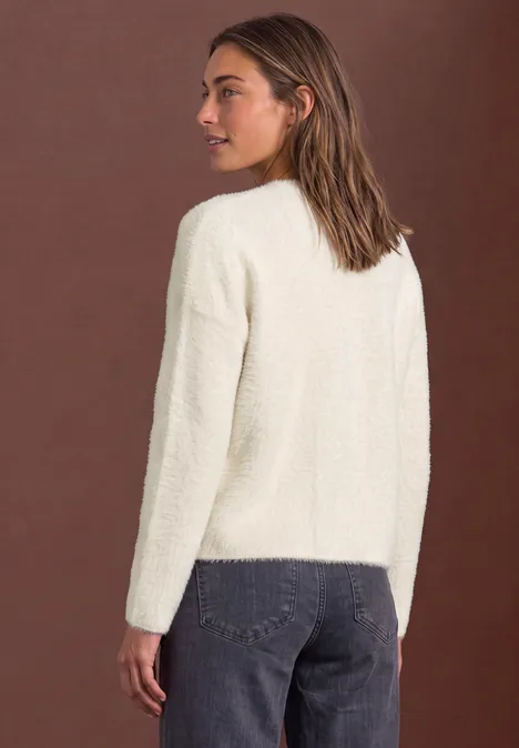 Femme portant un pull duveteux crème et un jean devant un fond marron