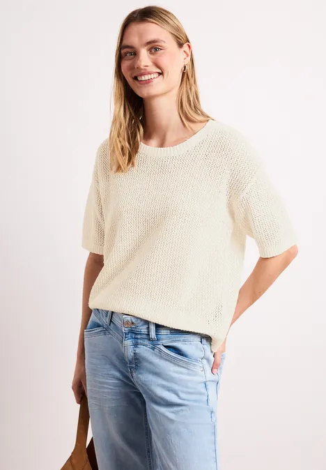 Frau in lockerem cremefarbenem Strickpullover mit kurzen Ärmeln und hellblauer Jeans