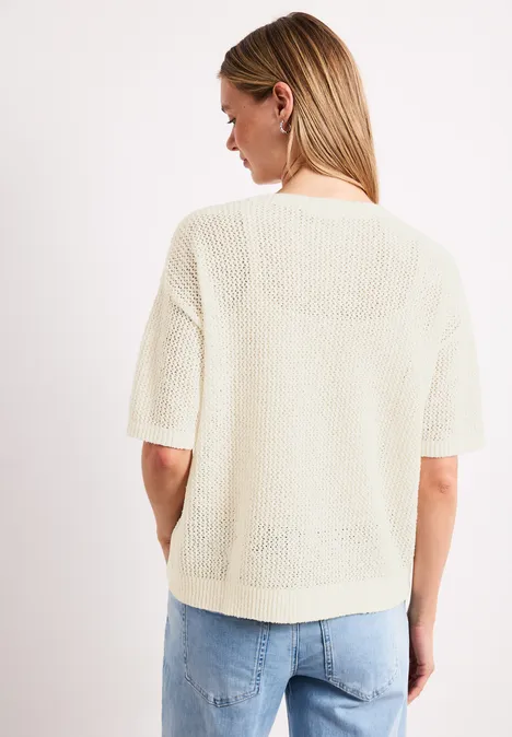 Frau von hinten in hellem, kurzärmligem Strickoberteil und Jeans vor weißem Hintergrund.