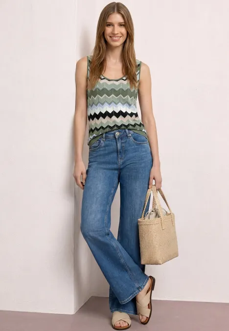 Vrouw in kleurrijk zigzagtop, wijdvallende jeans, sandalen, met een linnen tas.