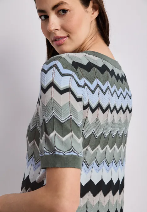 Person von hinten in kurzärmeligem Oberteil mit mehrfarbigem Zickzack-Muster.