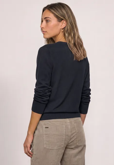 Rückansicht einer Frau in einem dunkelblauen Pullover und beigen Hosen.