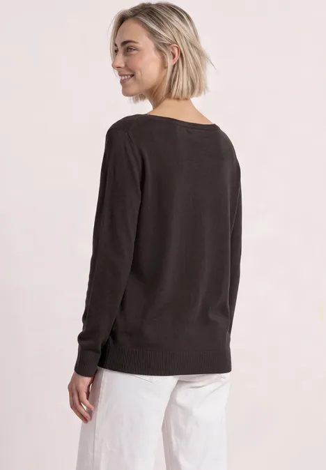 Eenvoudige trui met boothals black coffee Frau mit kurzem blonden Haar trägt einen dunkelbraunen Pullover und weiße Hose, lächelt und schaut zurück.
