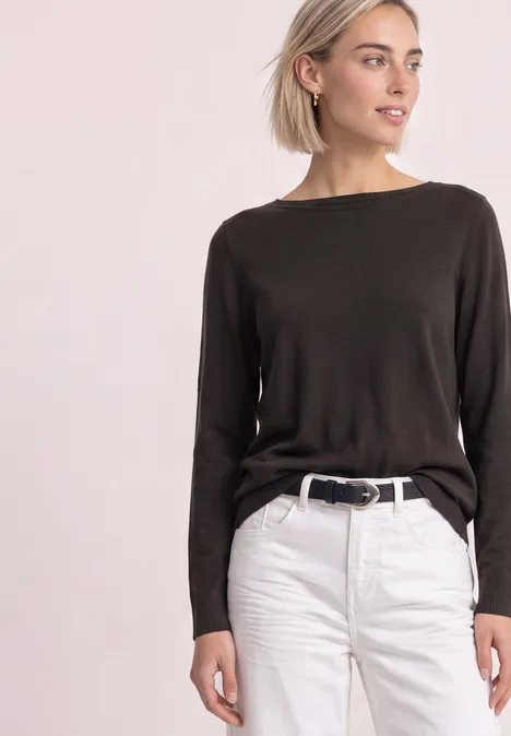 Eenvoudige trui met boothals black coffee Frau in kastanienbraunem Pullover mit langen Ärmeln und weißen Jeans, schwarzem Gürtel vor hellem Hintergrund.