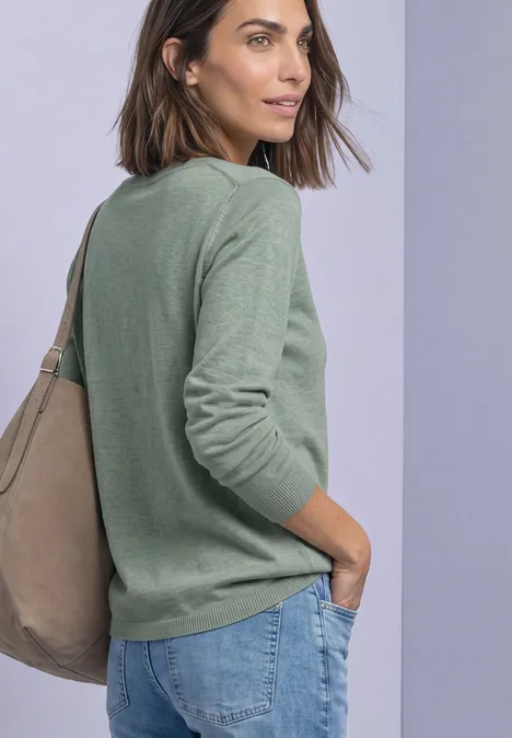 Eenvoudige trui met boothals eucalyptus green mel. Frau im Profil mit grünem Pullover, blauen Jeans und beiger Tasche über der Schulter