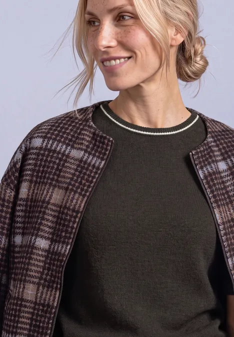 Pull à manches courtes avec détails contrastés black coffee mel. Nahaufnahme einer lächelnden Frau im grünen Pullover mit karierter Jacke über den Schultern.