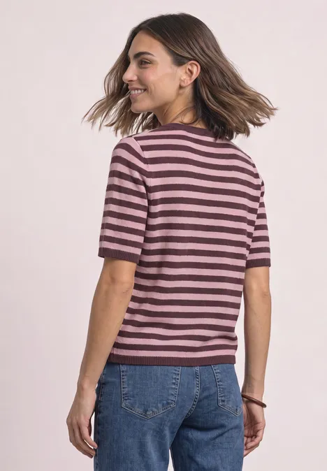 T-shirt met korte mouwen, ronde hals en strepen rustic rouge mel. Frau trägt rosa-bordeaux gestreiftes T-Shirt und blaue Jeans, dreht sich lächelnd zur Seite.