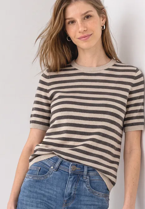 T-shirt met korte mouwen, ronde hals en strepen clay sand mel. Junge Frau in gestreiftem Kurzarmshirt und Jeans lehnt lässig an einer Wand.