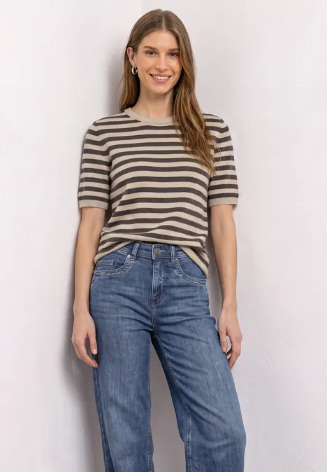 T-shirt met korte mouwen, ronde hals en strepen clay sand mel. Eine junge Frau trägt ein gestreiftes T-Shirt und Jeans, sie lächelt entspannt.