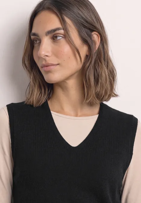 Pullunder mit V-Neck in Unifarbe Black Frau in schwarzer Strickweste mit V-Ausschnitt über beigem Shirt, seitlich blickend.