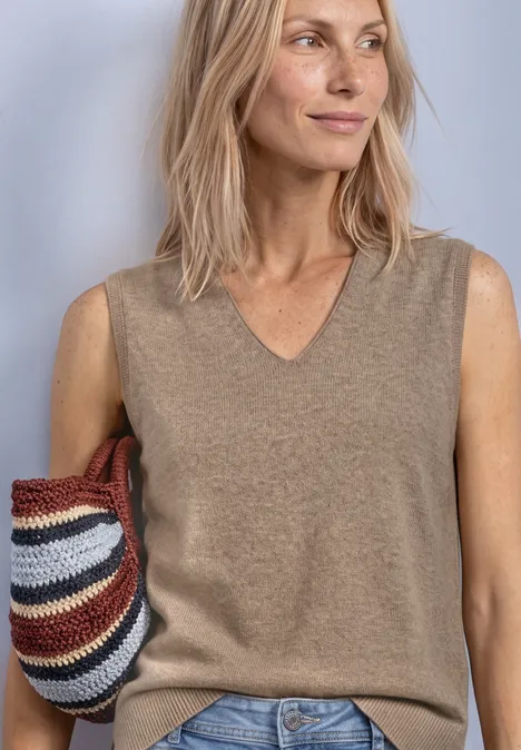 V-hals trui in effen kleur sanded amber mel. Frau in beigem Ärmellosen Pullover und Jeans hält eine mehrfarbige Strohtasche.