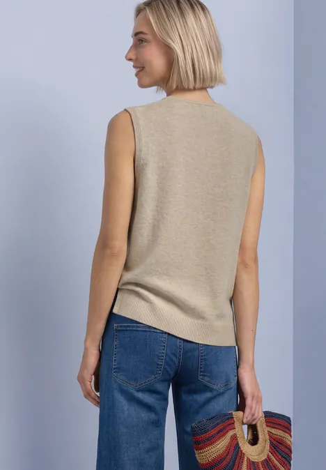 V-hals trui in effen kleur light sepia sand mel. Frau von hinten trägt ein beiges ärmelloses Top, blaue Jeans und hält einen bunten Korb.