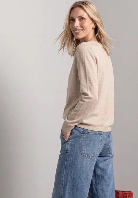 Eenvoudige trui met boothals clay sand mel. Frau mit beigem Pullover und weiten Jeans, sieht lächelnd über die Schulter.